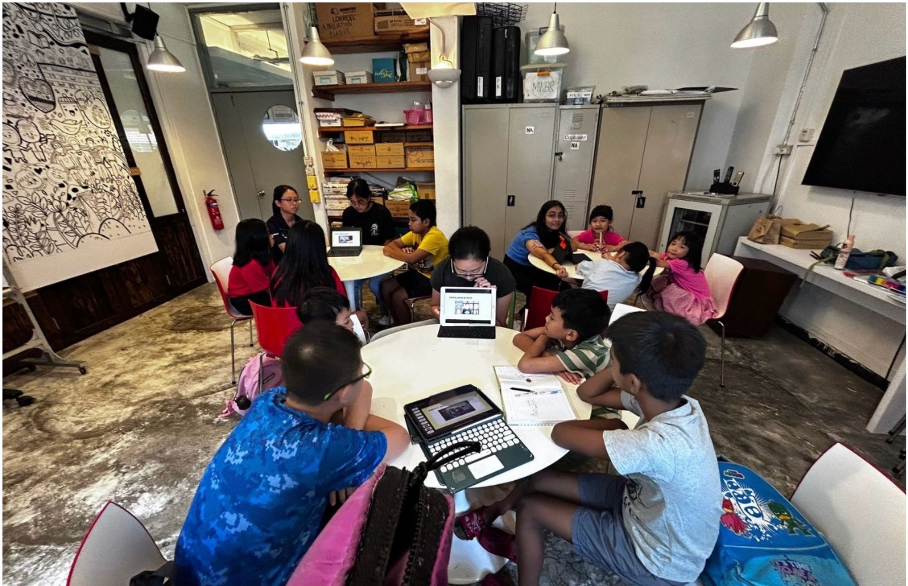 Children working on tablets around low tables with Project STEMulate volunteers during a workshop